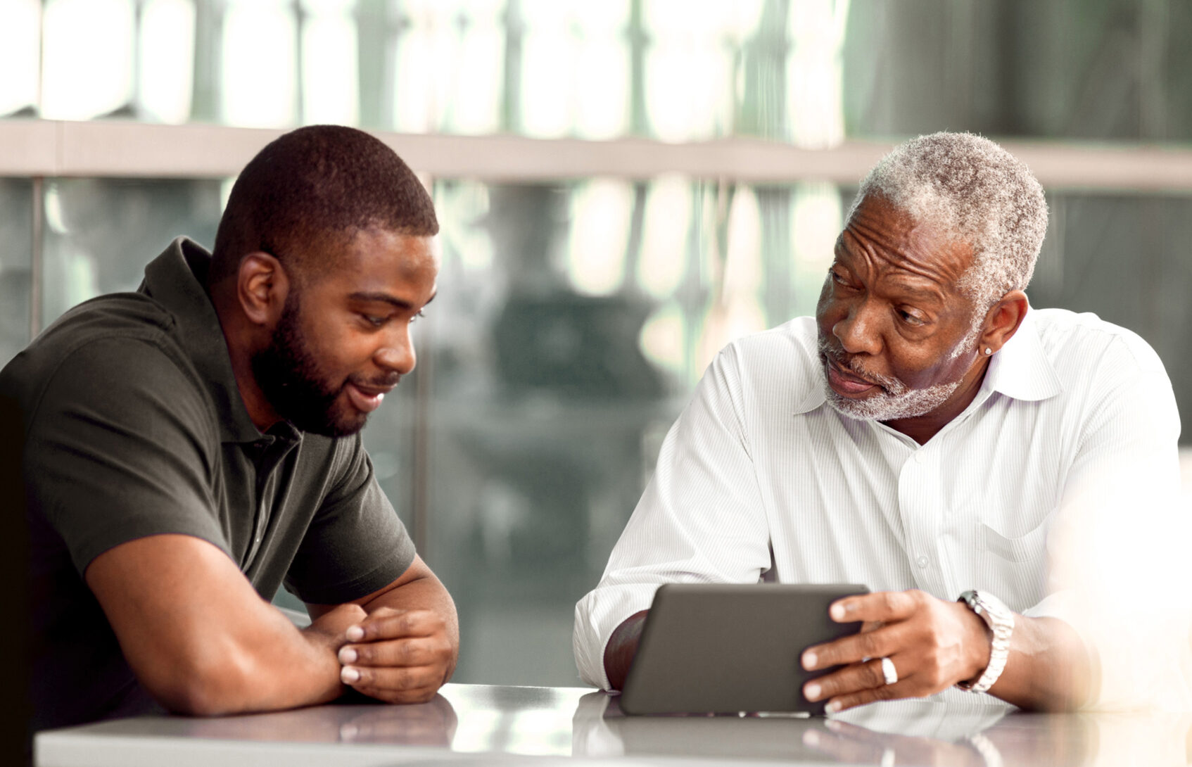 Two men, father and son, discuss something they are viewing online