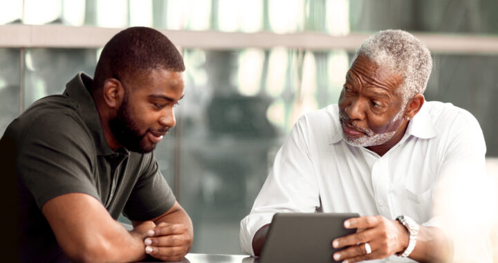 Two men, father and son, discuss something they are viewing online