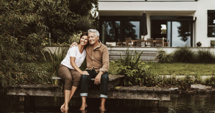 Smiling senior man sitting with arm around woman on jetty by lake