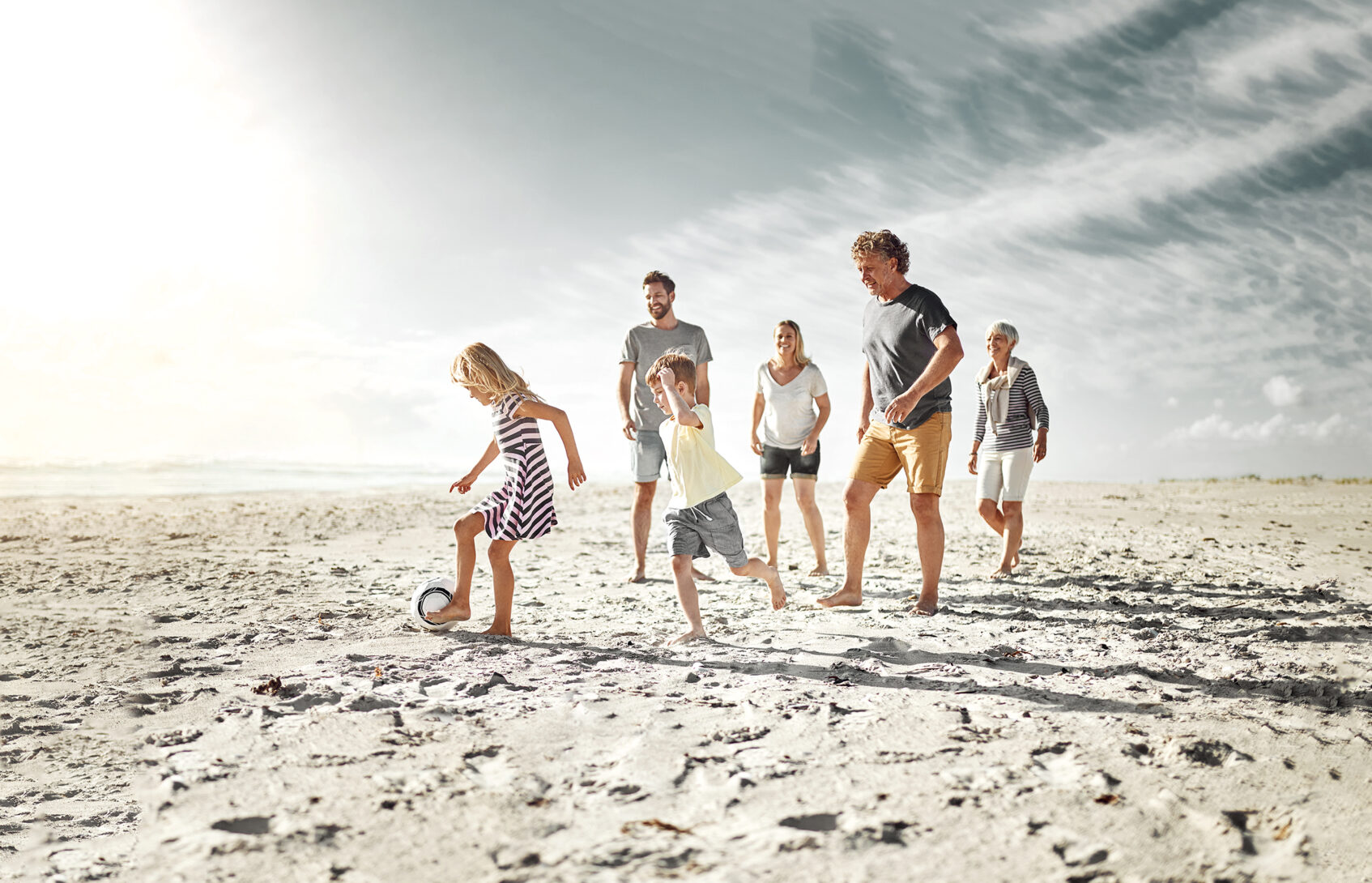 Multi-generational family playing with a ball on the beach.