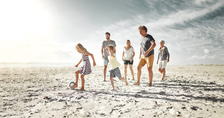 Multi-generational family playing with a ball on the beach.