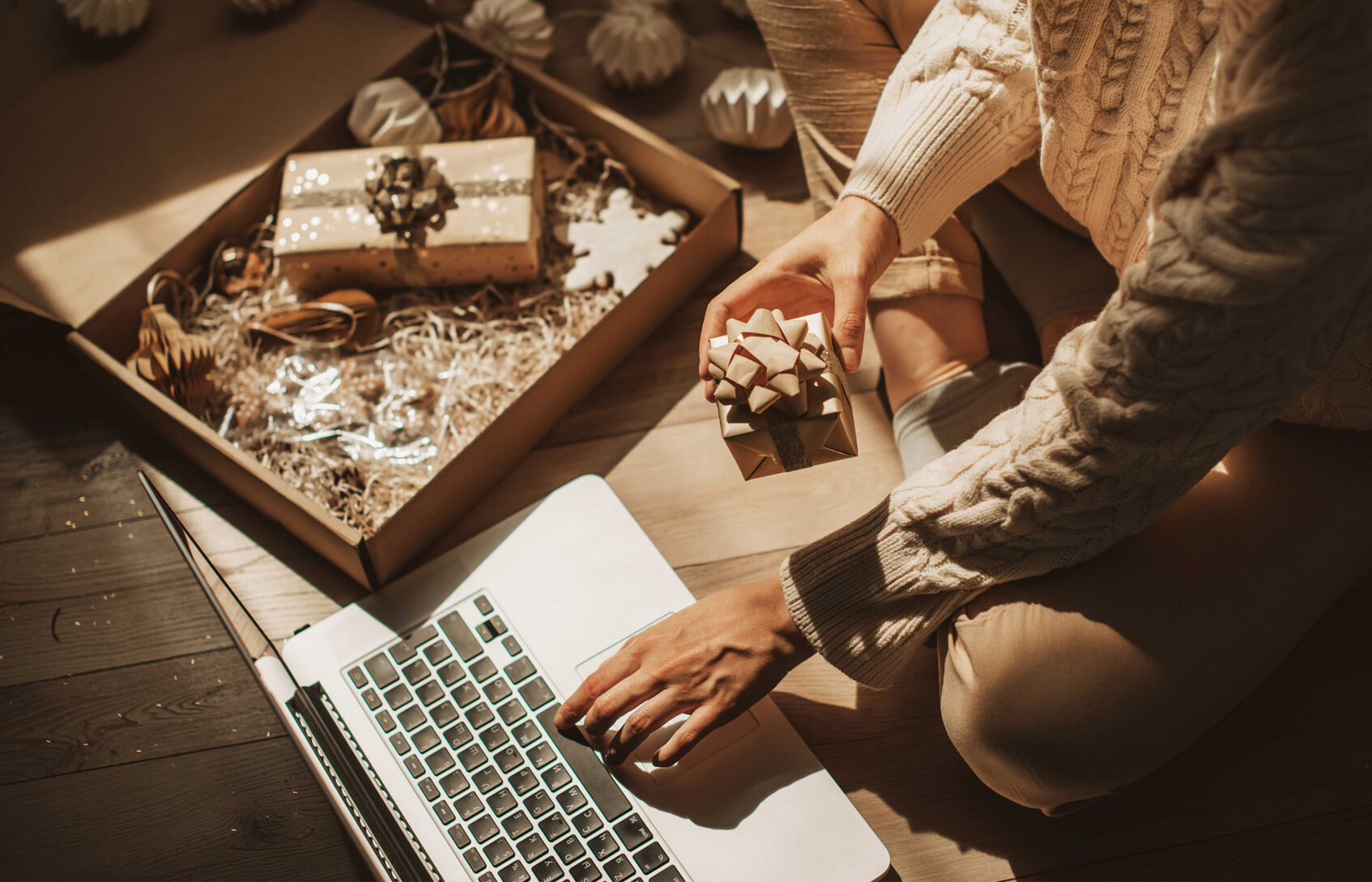 Woman seated on the floor with a gift box in hand and a laptop.