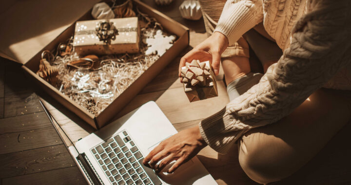 Woman seated on the floor with a gift box in hand and a laptop.